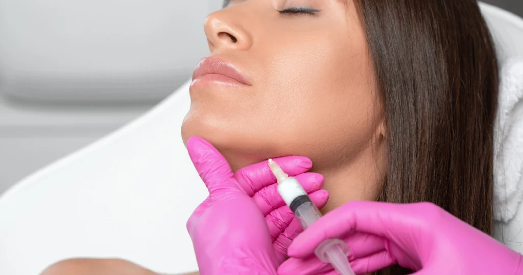 Woman receiving a Kybella chin injection from a professional in pink gloves in Carmel IN